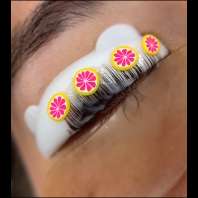 Olho com pestanas postiças em almofada branca e autocolantes amarelos e rosa