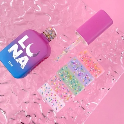 Frasco de verniz de unha azul e rosa com amostras de unhas com confetes coloridos