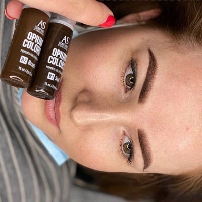 Mulher jovem com sobrancelhas castanhas claras segurando dois frascos de cor para sobrancelhas.