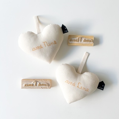 Dois corações de tecido branco bordados com nomes e carimbos de madeira