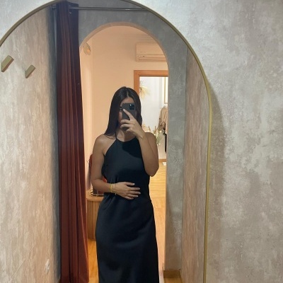 Vestido preto comprido de cetim com alças finas num espelho arqueado dourado