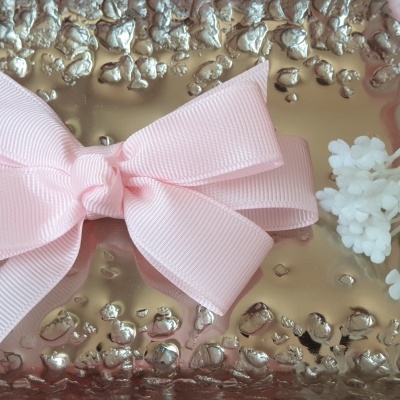 Laço rosa claro sobre superfície metálica dourada com flores ao lado