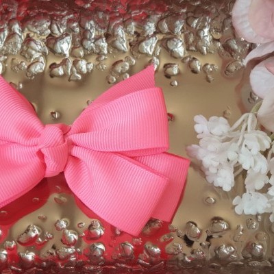 Laço cor-de-rosa em bandeja metálica com flores brancas e folhas cor-de-rosa