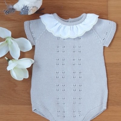 Body de bebé cinzento claro com gola branca bordada, em fundo de madeira com pássaro e flores.