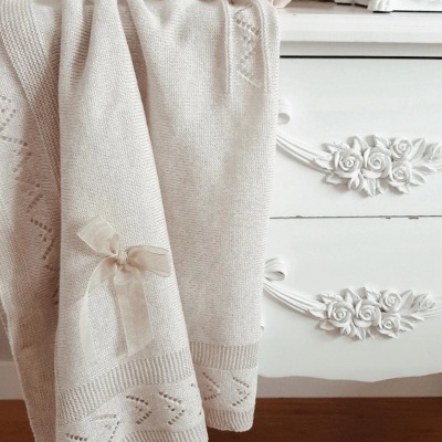 Manta de malha bege clara com laço sobre cómoda branca decorativa com moldura de fotografia ao fundo