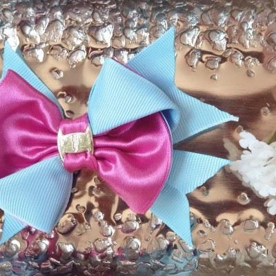 Laço azul claro com laço rosa e detalhe dourado sobre superfície prateada com flores