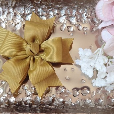 Laço amarelo mostarda sobre superfície metálica com flores brancas e rosa