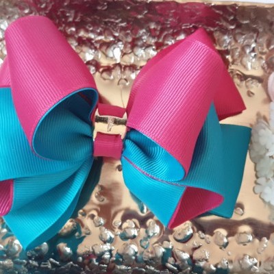 Laço para cabelo rosa e azul turquesa com fivela dourada sobre superfície metálica e flores