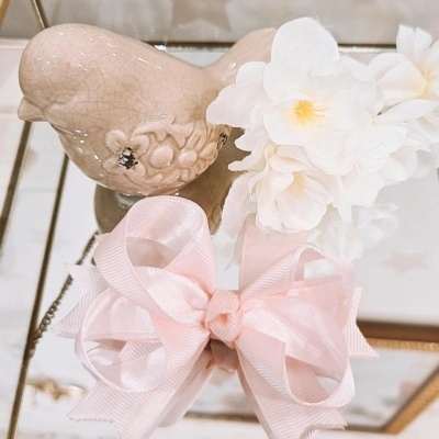 Pássaro cerâmico bege, flores brancas artificiais e laço rosa decoram superfície espelhada.