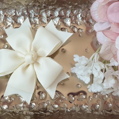 Laço creme de tecido sobre superfície metálica prateada e flores artificiais