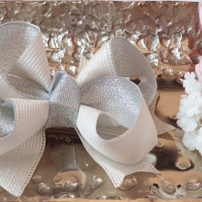 Laço decorativo branco e prateado sobre bandeja metálica com flores ao lado