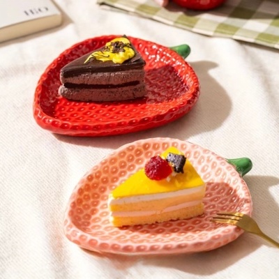 Duas fatias de bolo em pratos cerâmicos vermelhos e rosa com padrão de morango.