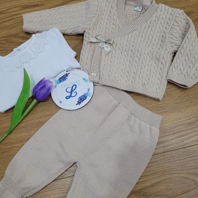 Conjunto de roupa para bebé creme com body branco e tulipa roxa sobre chão de madeira.