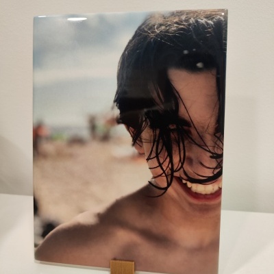 Foto emoldurada de pessoa sorridente com cabelo molhado e fundo de praia desfocado