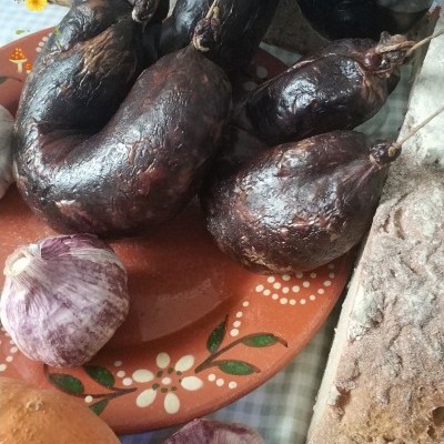 Prato com enchidos pretos, alho, pão e copo de vinho tinto sobre toalha xadrez
