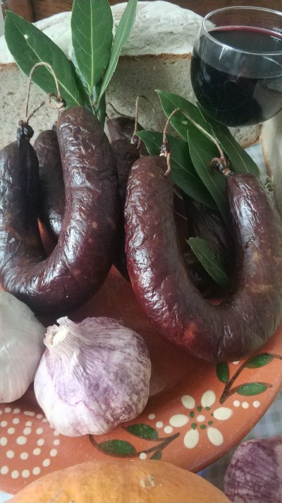 Chouriços, alhos, pão integral e copo de vinho tinto num prato decorativo