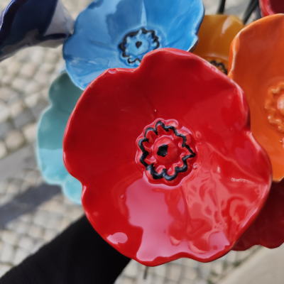 Flores cerâmicas coloridas esmaltadas sendo seguradas à mão