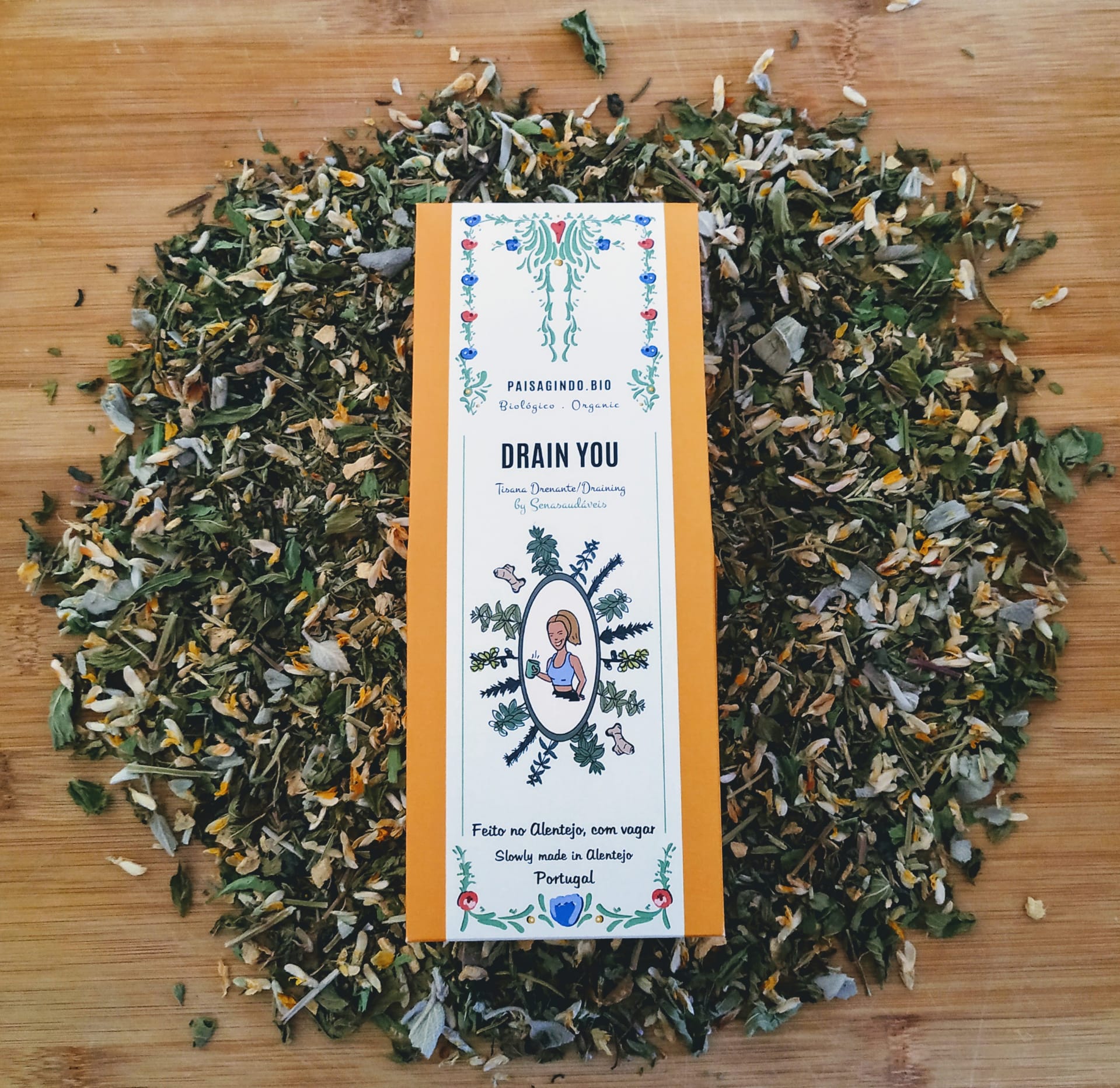 Pacote de chá Drain You rodeado por folhas de chá soltas em mesa de madeira