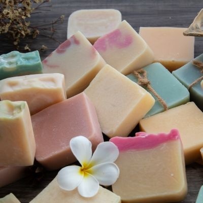 Barras de sabão artesanal em várias cores e texturas sobre madeira com flor branca e amarela