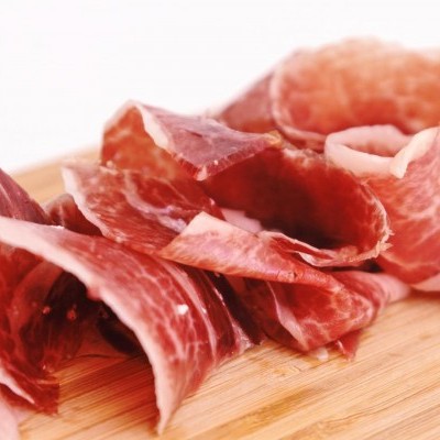 Fatias de presunto curado vermelhas sobre tábua de madeira clara.