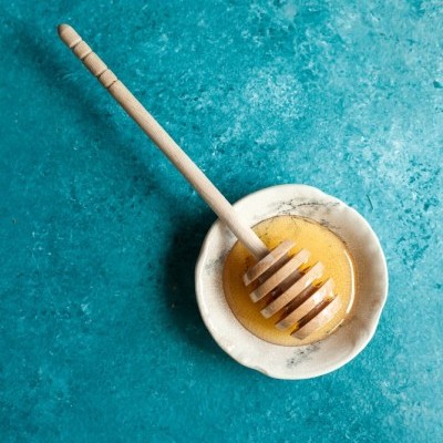 Colher de mel de madeira numa taça branca com mel sobre fundo azul