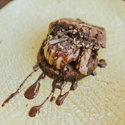 Sobremesa de biscoitos de chocolate com creme e cobertura de chocolate num prato bege texturizado