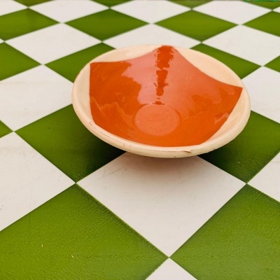 Prato raso cerâmico laranja e bege sobre superfície quadriculada verde e branca