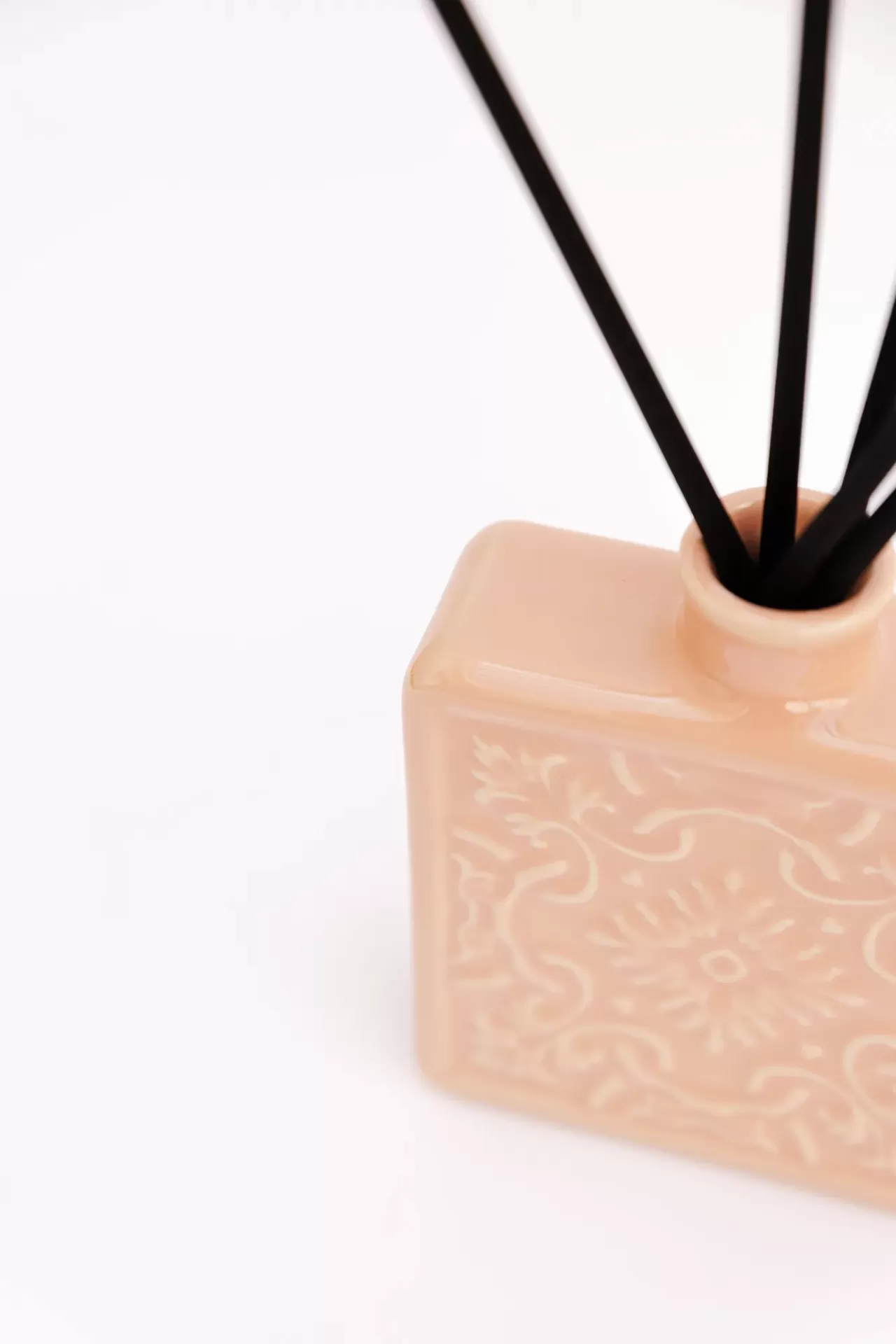 Recipiente de cerâmica bege com padrão floral e pauzinhos de difusor pretos