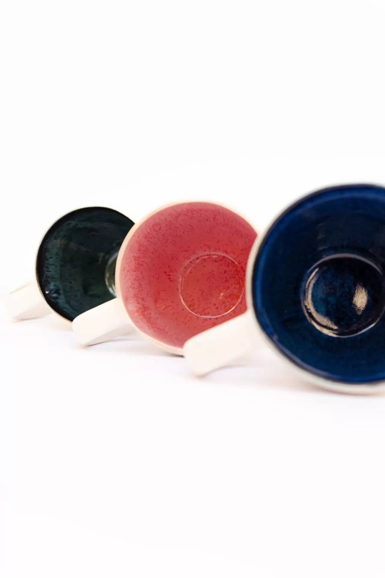 Três chávenas cerâmicas coloridas azul escuro, rosa e verde com suporte branco.