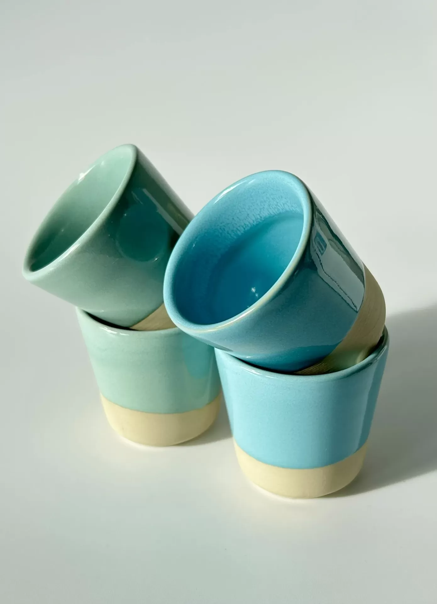 Quatro copos cerâmicos em tons azuis e verdes com base branca