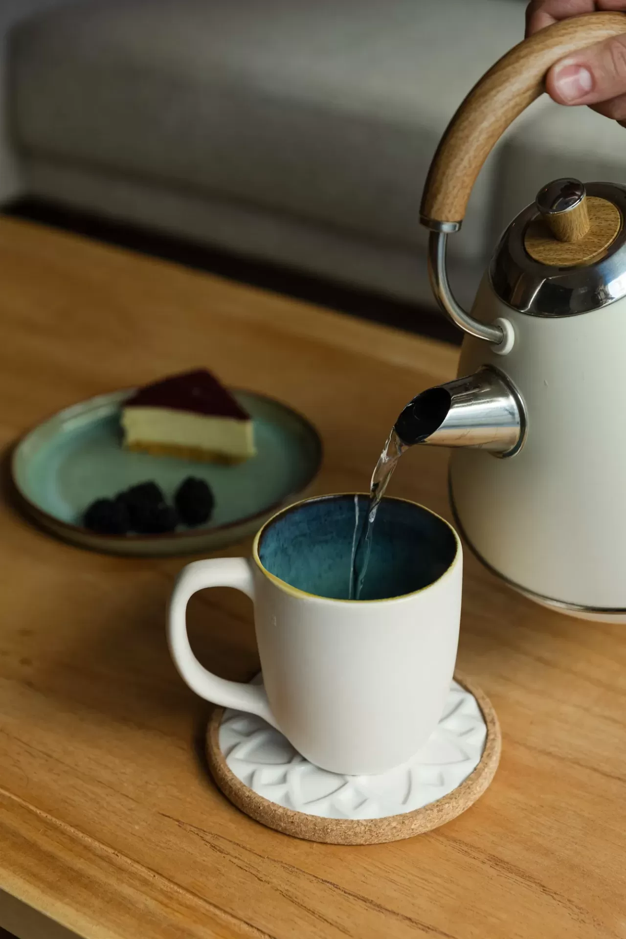 Caneca branca com interior azul e chaleira branca a verter água numa mesa de madeira