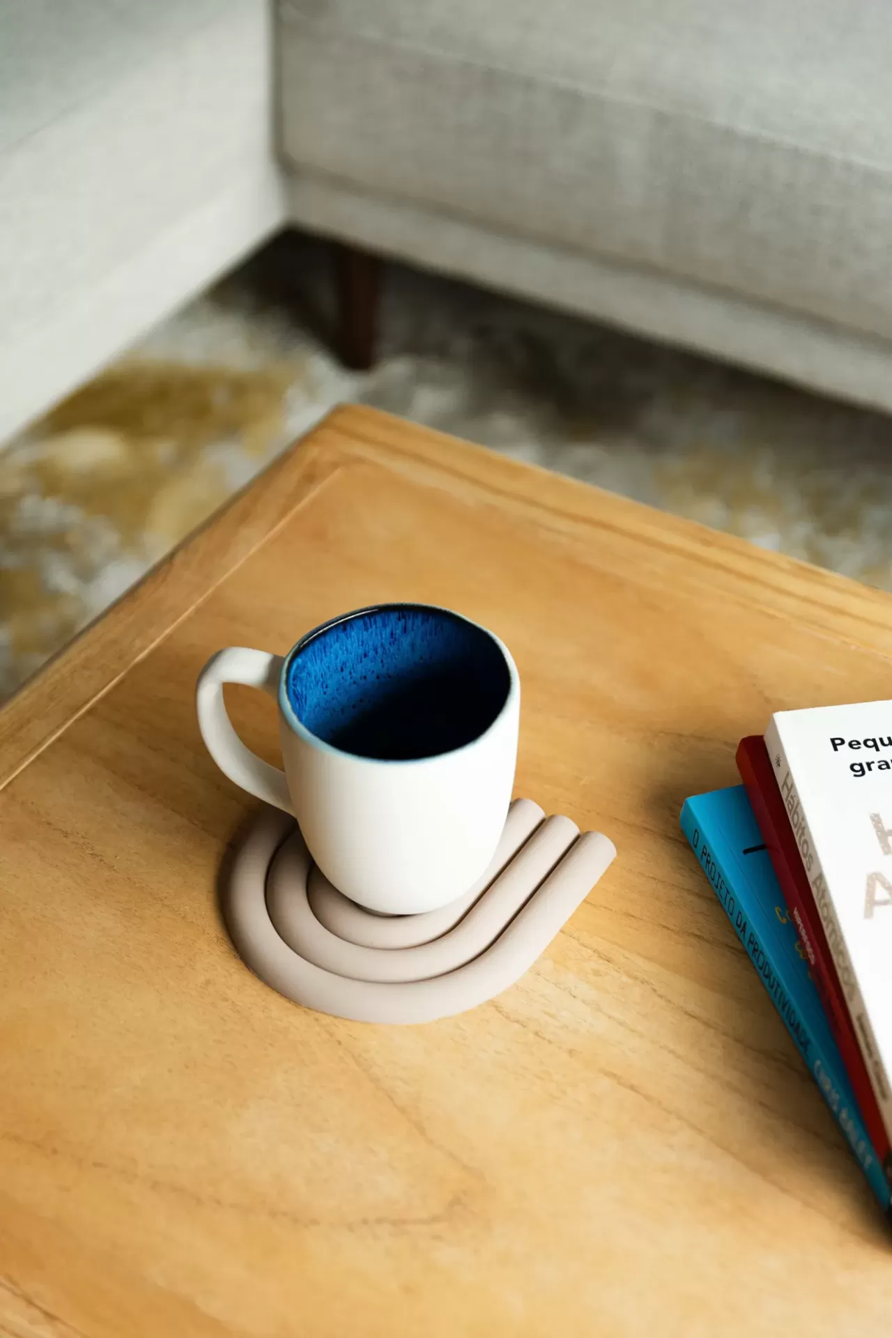 Chávena branca com interior azul escuro numa base de silicone sobre mesa de madeira com livro ao lado