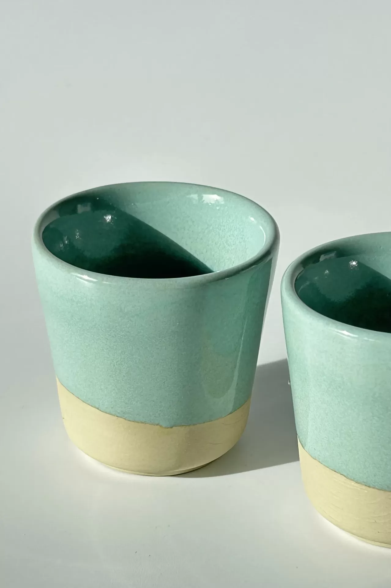 Dois copos de cerâmica azul clara e bege em superfície branca