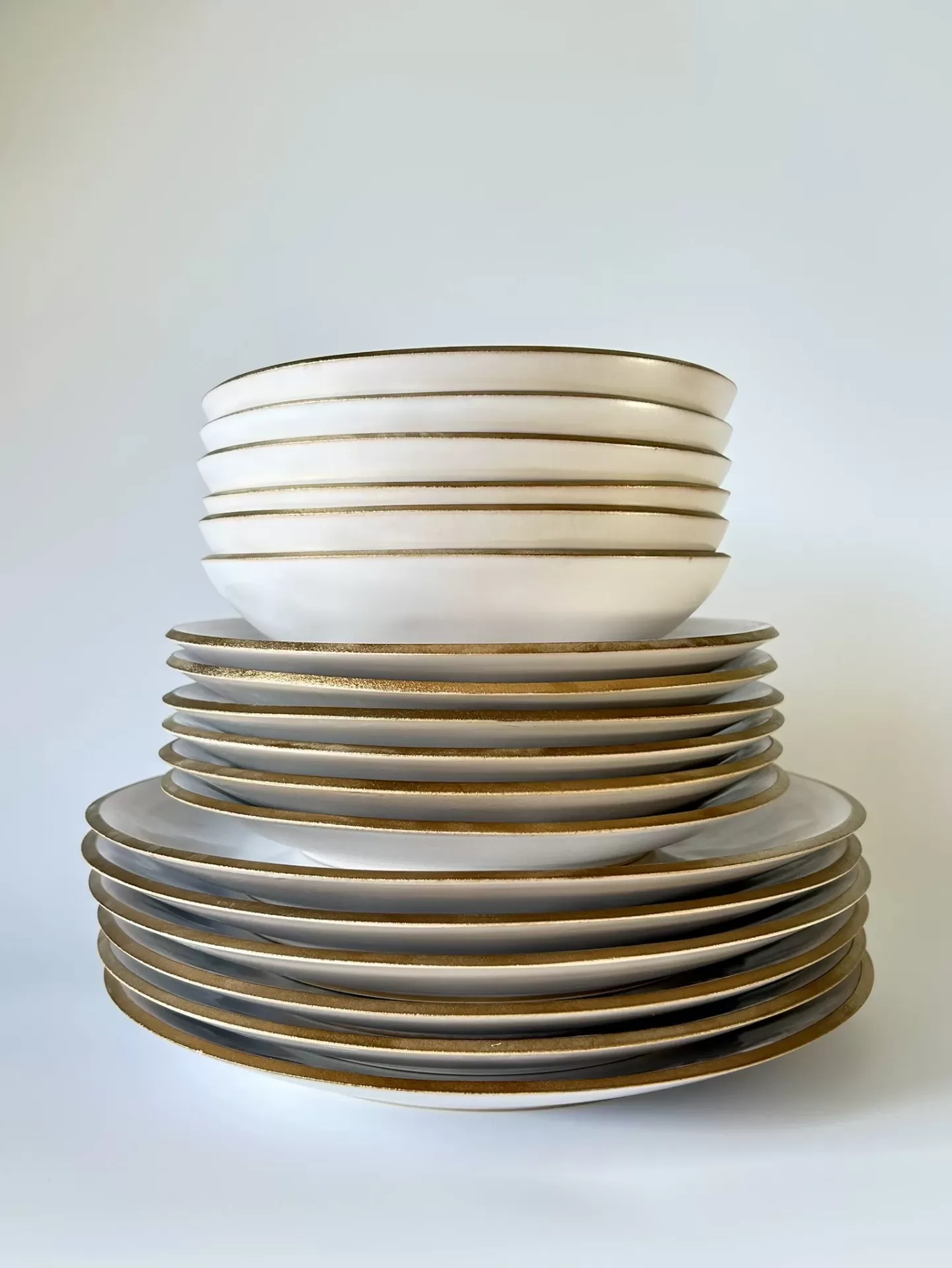 Conjunto de pratos e tigelas em cerâmica branca com bordas douradas empilhados