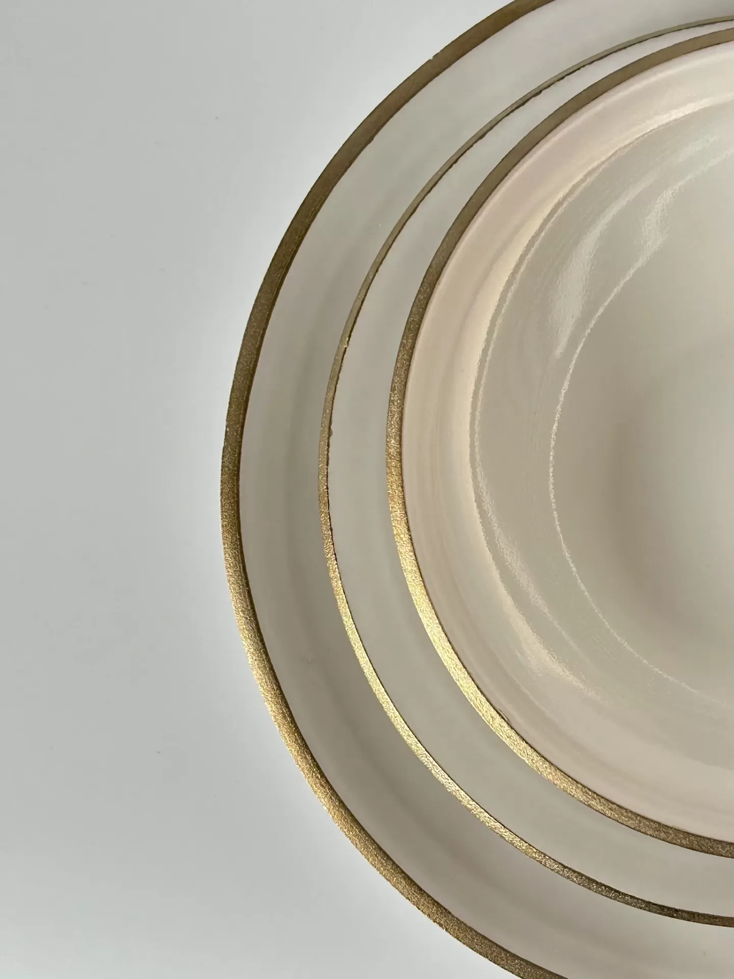Três pratos cerâmicos creme com bordas douradas sobre superfície branca