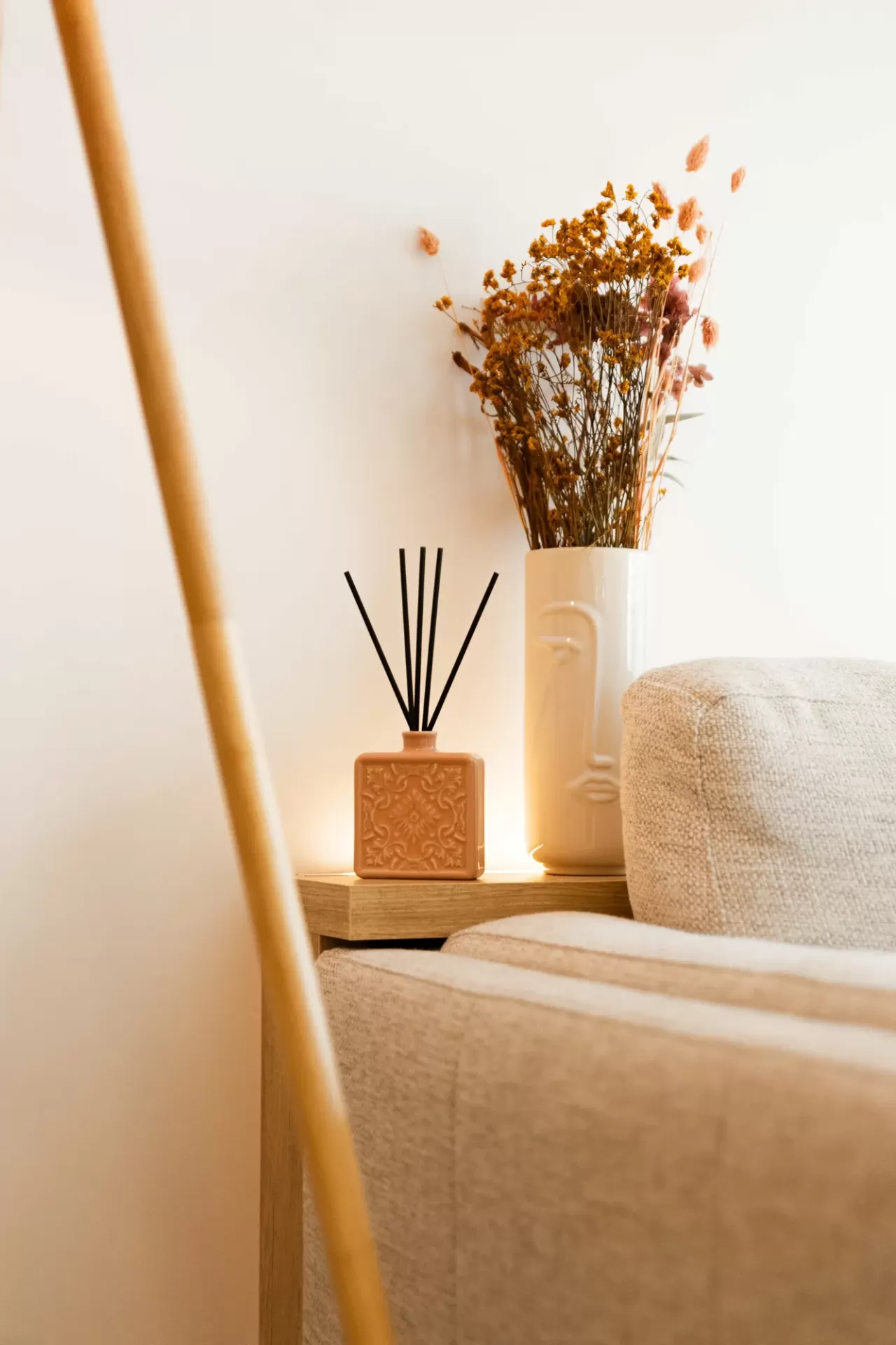 Frasco perfumado e vaso decorativo com flores em mesa de madeira ao lado de sofá bege