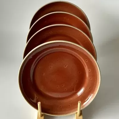 Conjunto de quatro pratos cerâmicos castanho-avermelhados com bordas bege em suporte de madeira