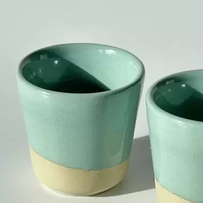 Dois copos de cerâmica azul clara e bege em superfície branca