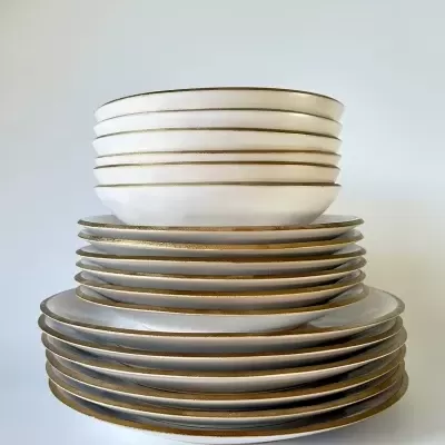 Conjunto de pratos e tigelas em cerâmica branca com bordas douradas empilhados