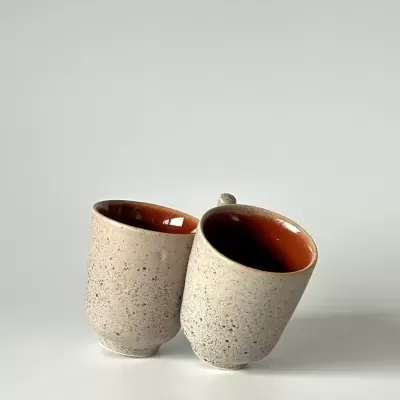 Dois copos de cerâmica cinza claro com interior laranja-avermelhado inclinados encostados.