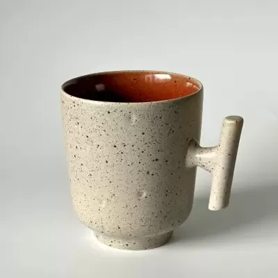 Caneca de cerâmica bege com interior castanho e pega cilíndrica.