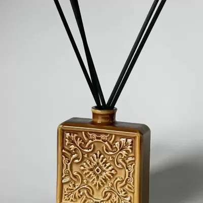 Difusor de aroma castanho em cerâmica com quatro varetas pretas finas.