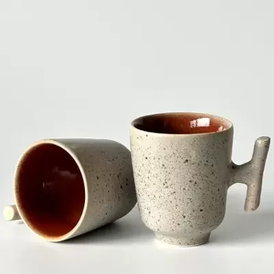 Duas chávenas de cerâmica cinzentas com interior laranja, uma de pé e outra deitada