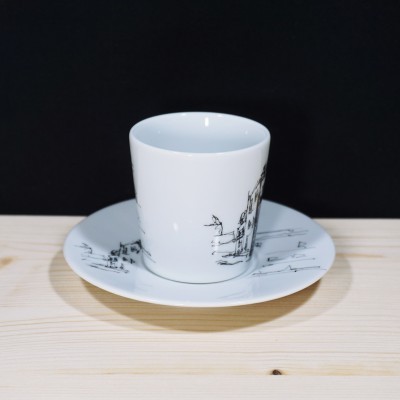 Chávena de porcelana branca com desenho preto sobre prato branco, em fundo preto