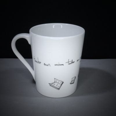 Caneca branca em cerâmica com desenhos a preto de jornais e texto escrito à mão.