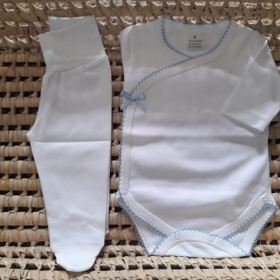 Conjunto branco de roupa de bebé com detalhes azuis sobre tecido trançado bege