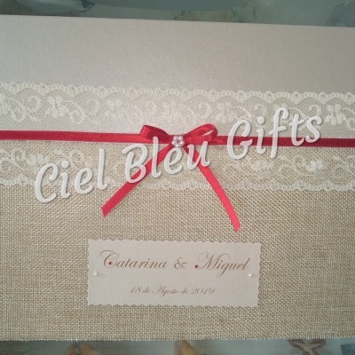 Livro de assinaturas com capa bege, renda branca e laço vermelho com texto Catarina & Miguel