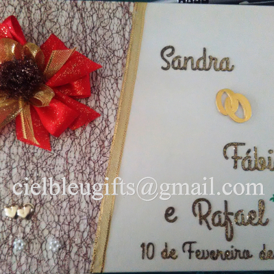 Livro decorativo branco com nomes dourados e um laço vermelho e dourado ao lado