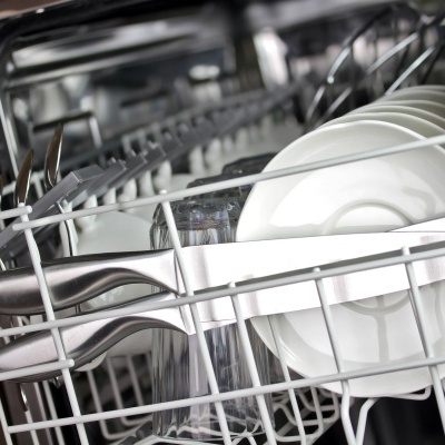 Interior de máquina de lavar louça com pratos brancos, talheres e copos.