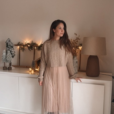 Mulher com camisola bege e saia rosa plissada em ambiente com decoração natalícia